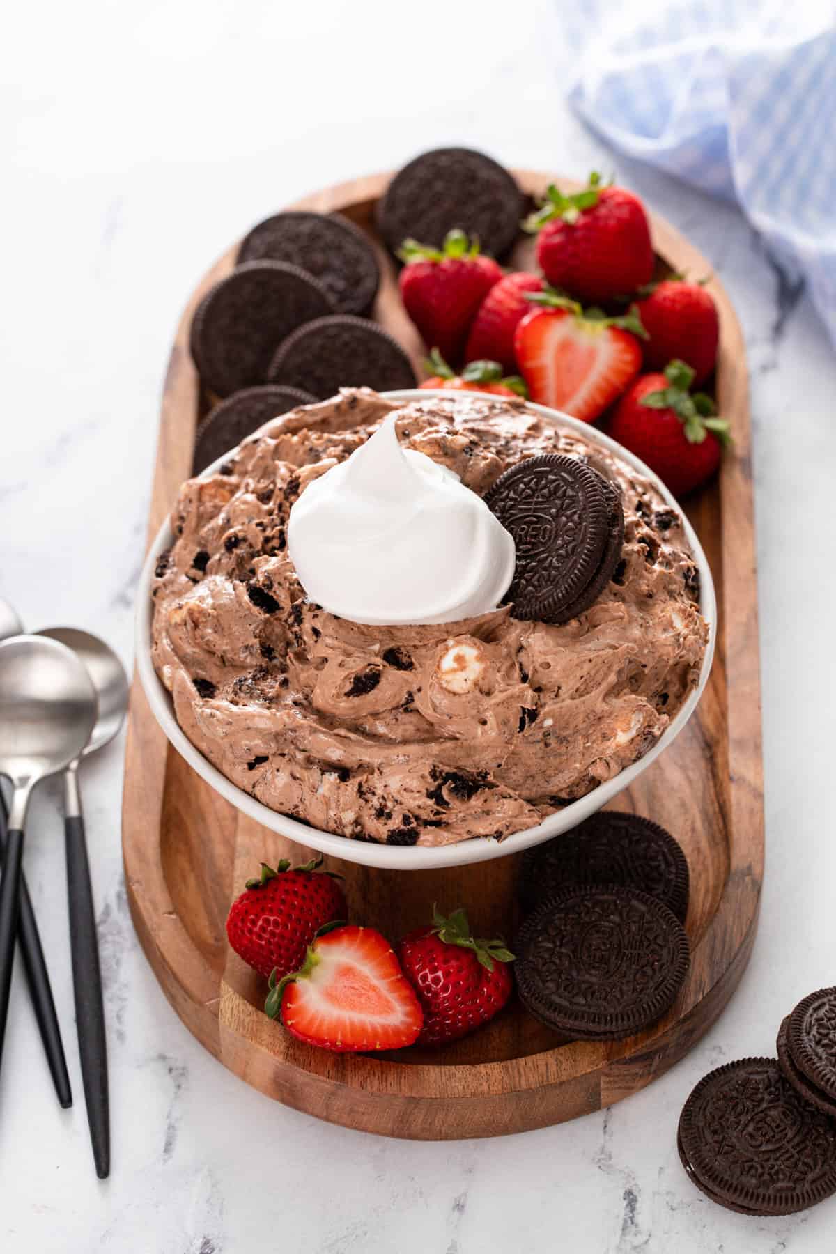 Bowl of oreo pudding topped with whipped cream and whole oreos, on a platter with oreos and fresh strawberries.