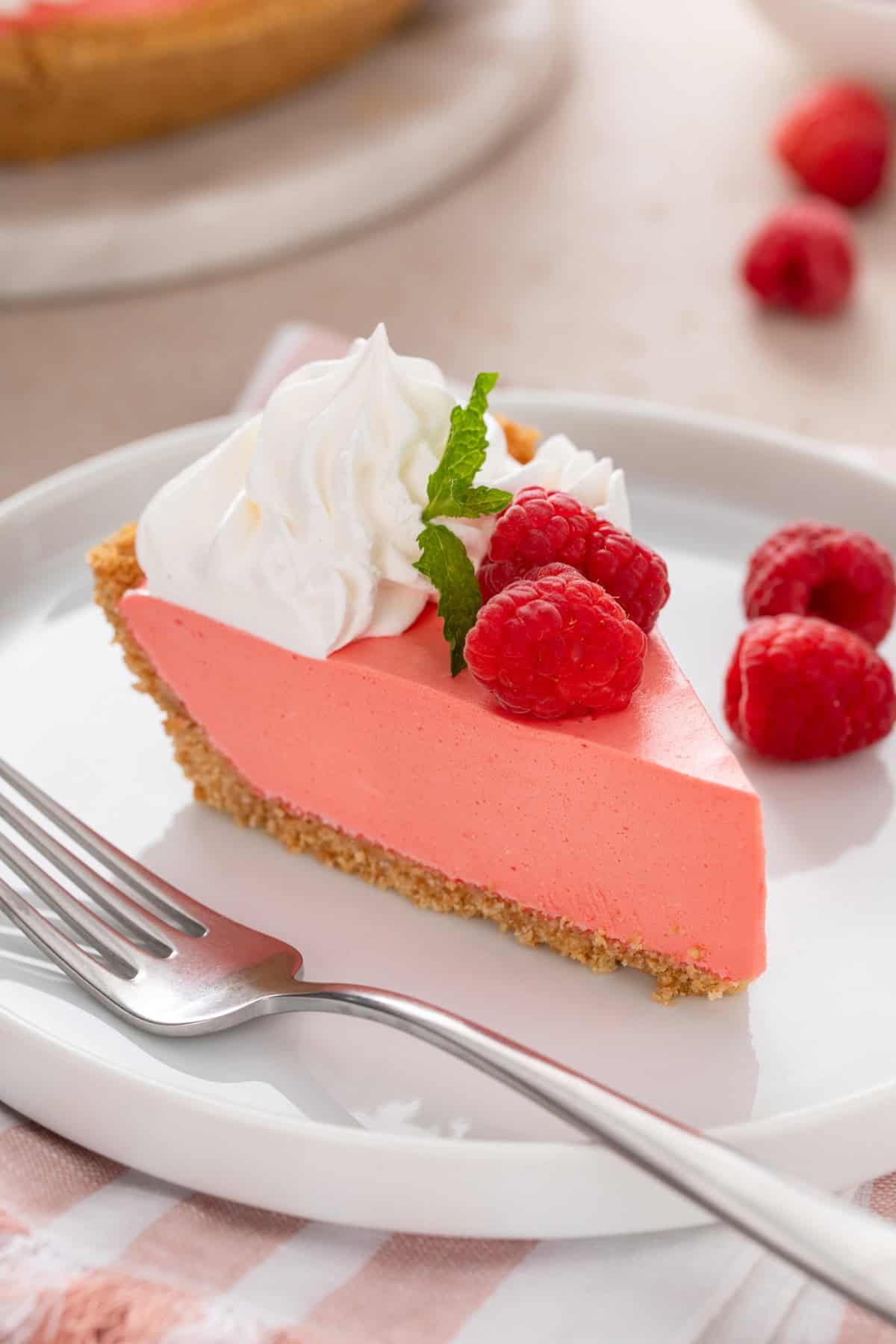 Close up of a slice of jello pie next to a fork on a white plate.