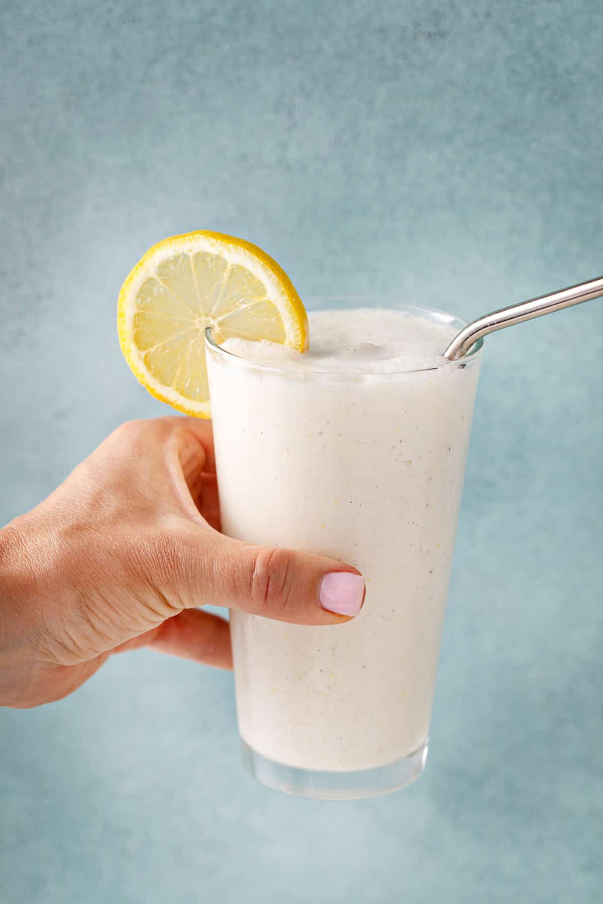 Hand holding up a glass of frosted lemonade in front of a blue background.