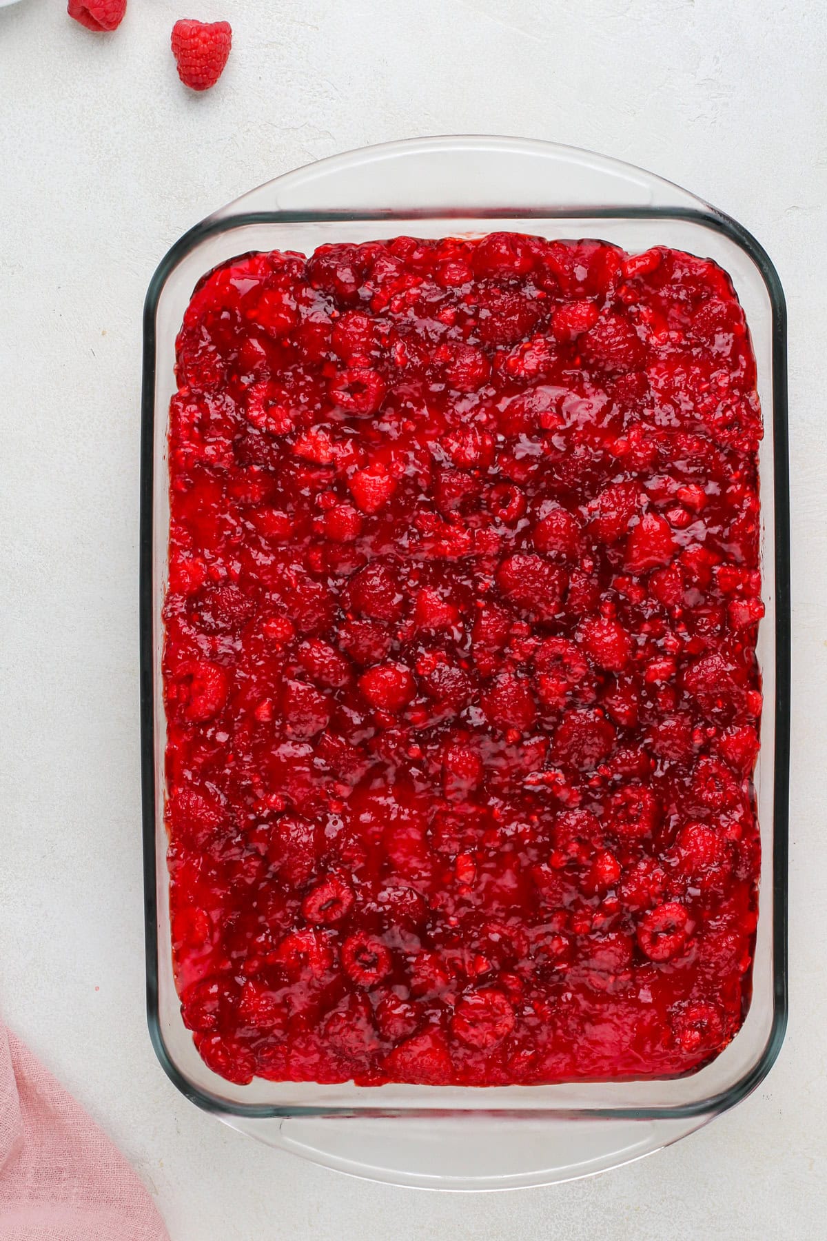 Raspberry jello layer spread onto cream cheese mixture in a baking pan.