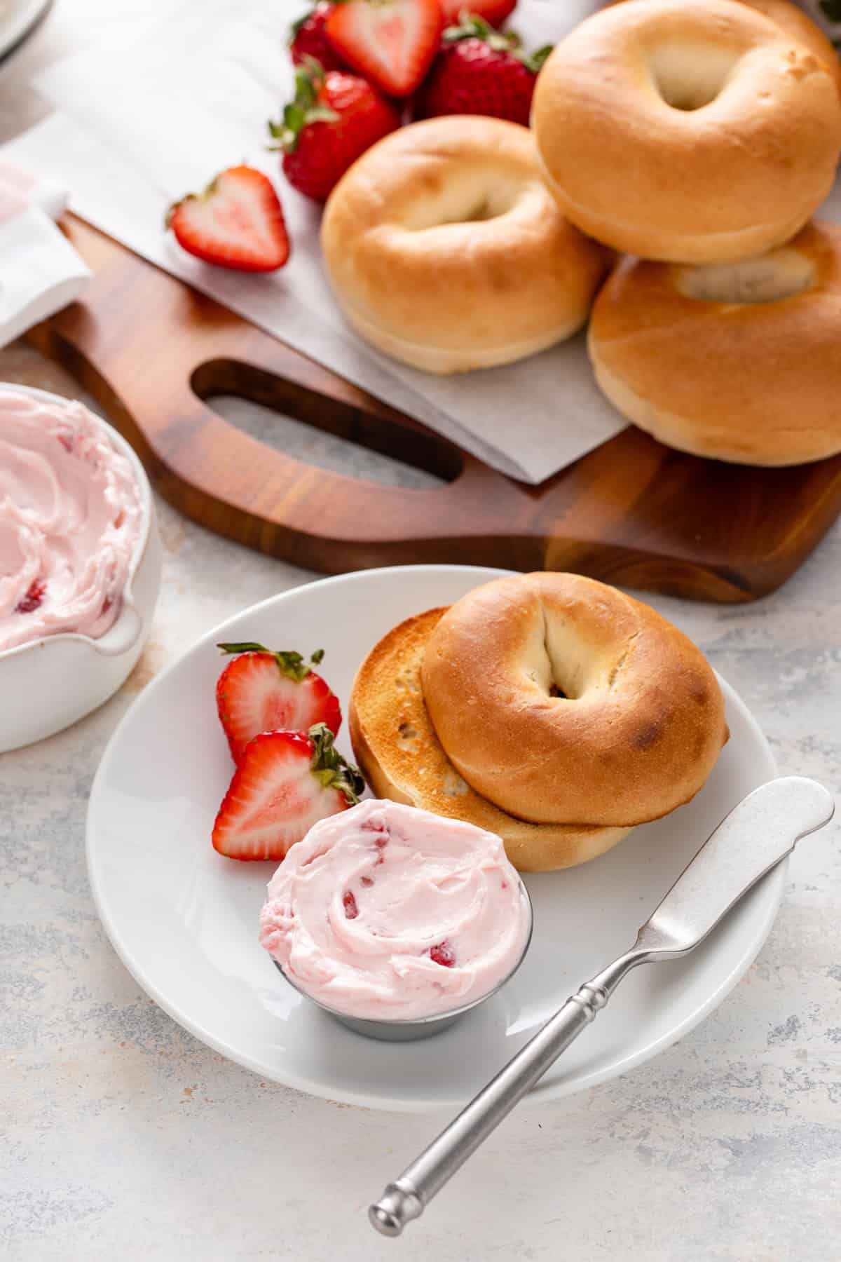 White plate holding a toasted bagel and a ramekin of strawberry cream cheese.