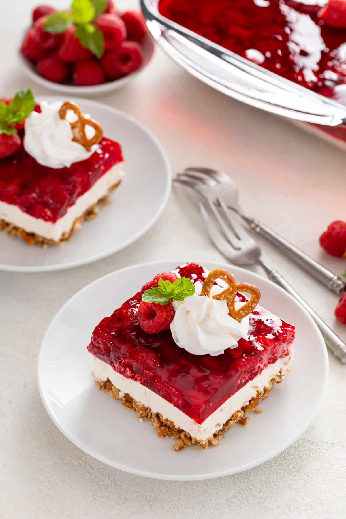 Two white plates holding slices of raspberry pretzel salad.