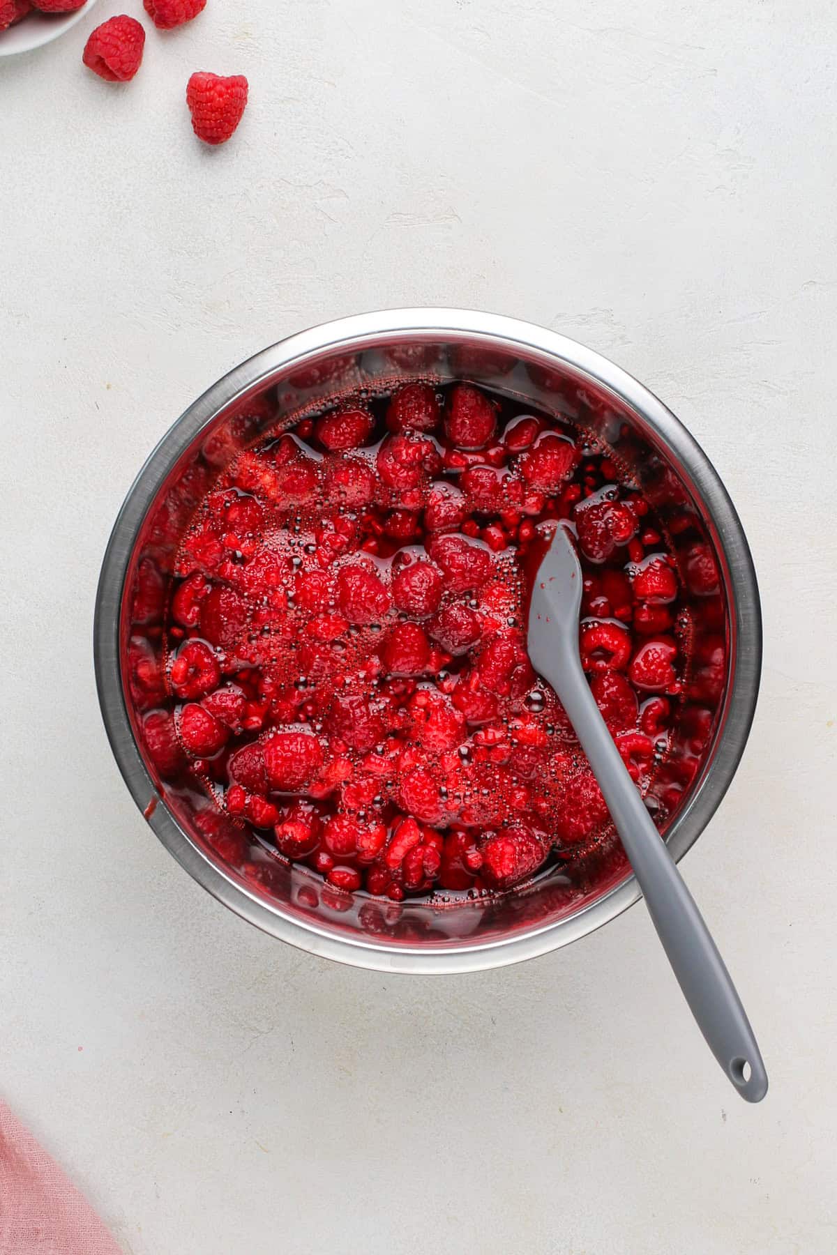 Frozen raspberries added to raspberry jello in a metal bowl.