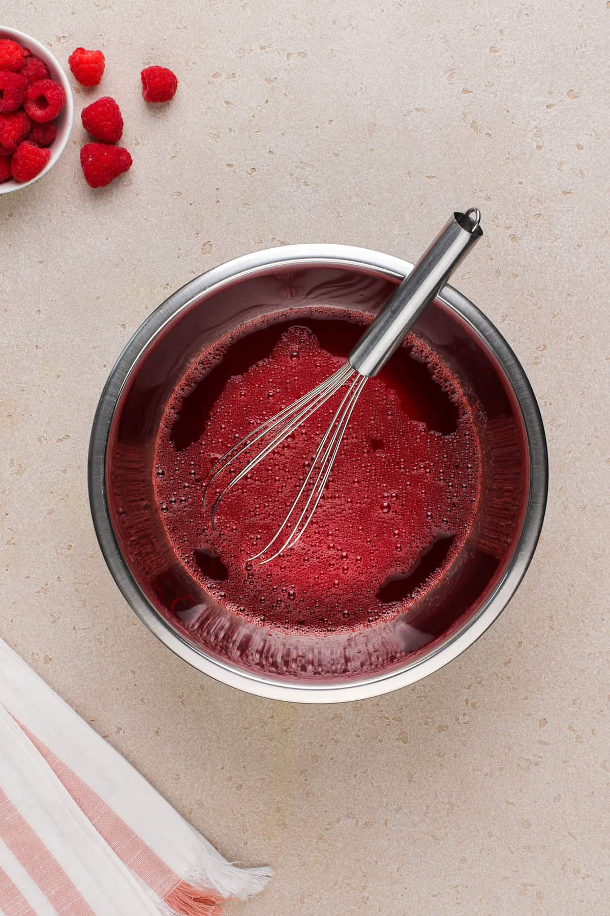 Raspberry jello whisked in a metal bowl.