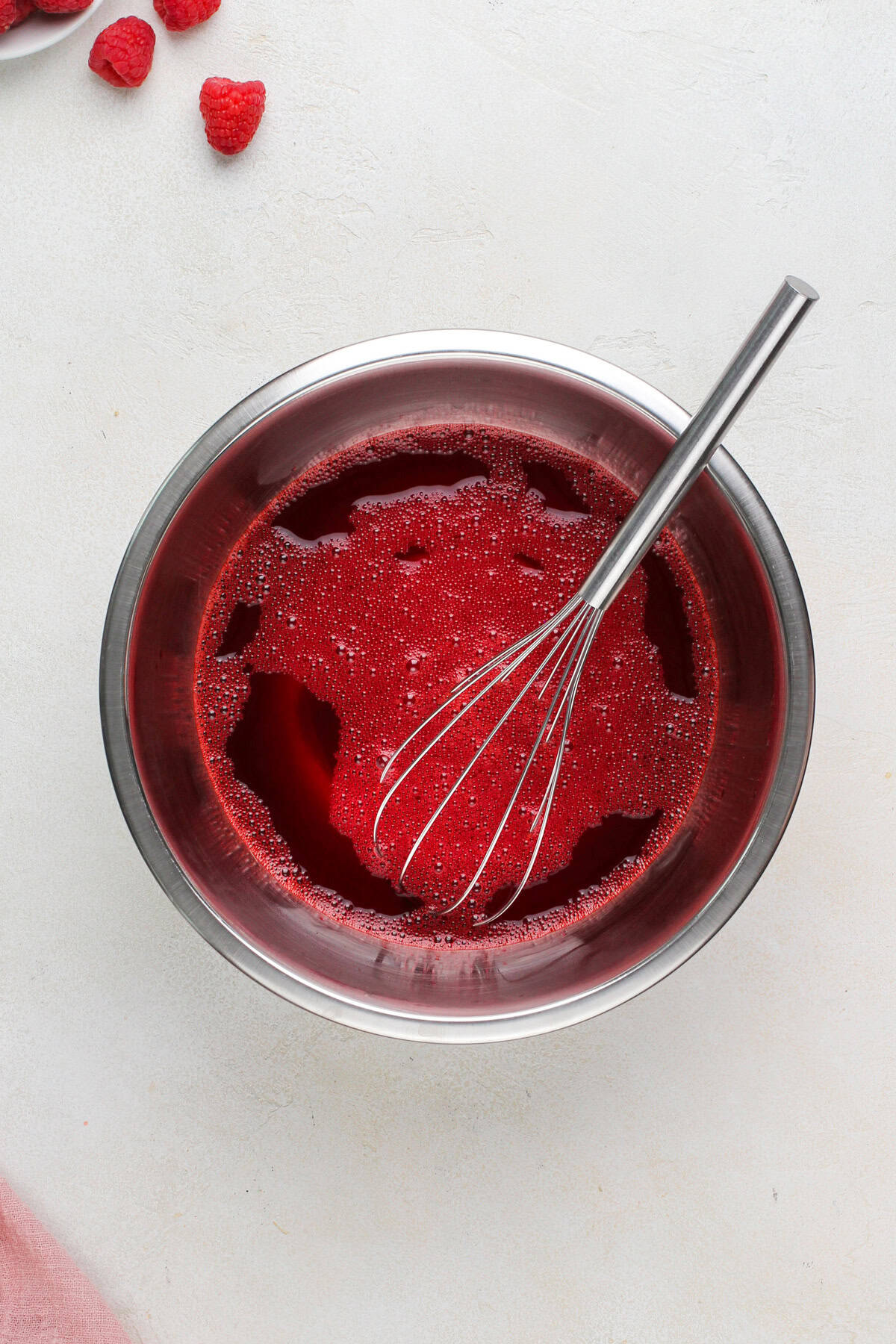 Raspberry jello whisked in a metal bowl.