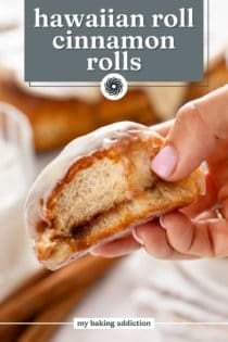 Hand holding up a hawaiian roll cinnamon roll with a bite taken from it. Text overlay includes recipe name.