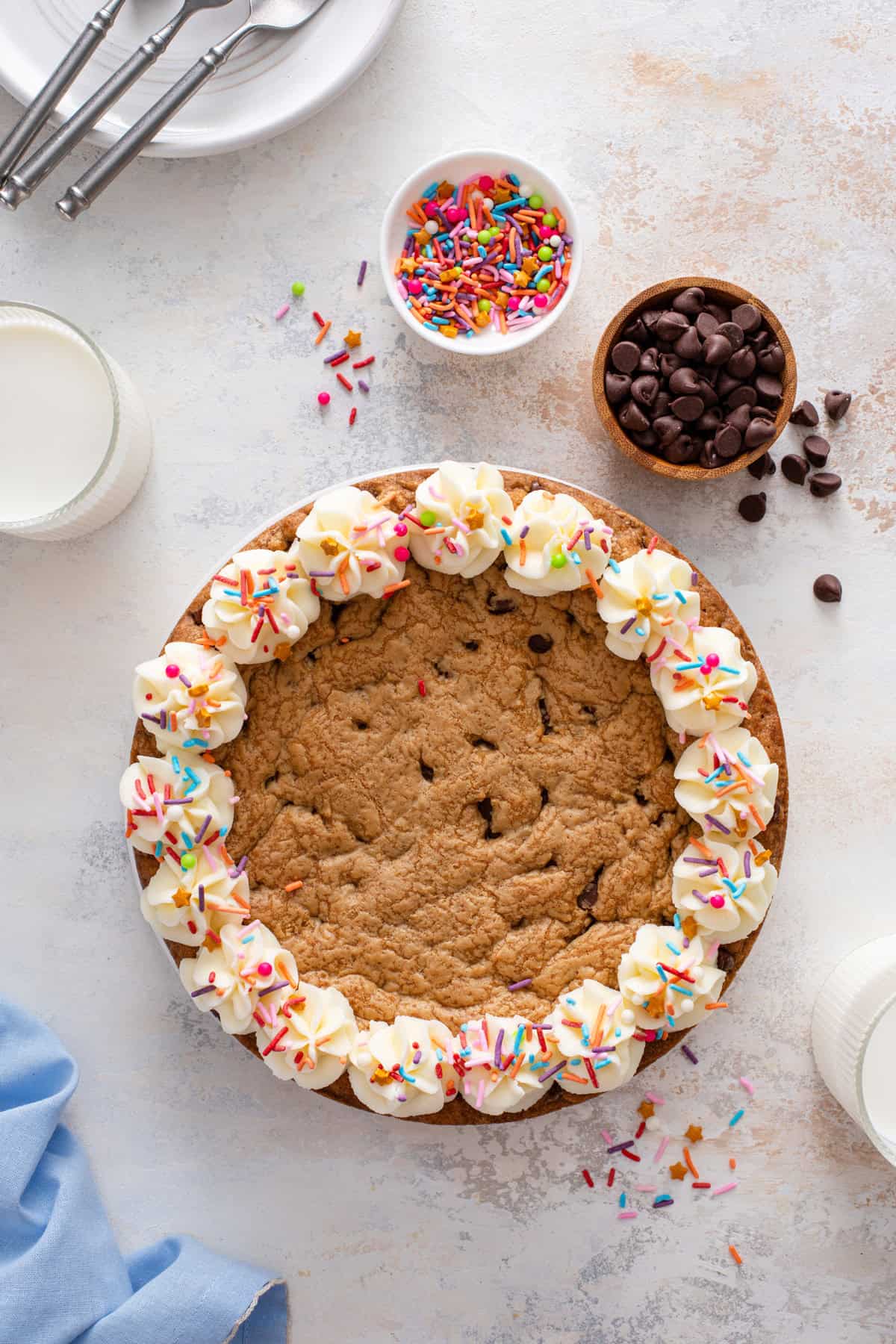 Overhead image of a chocolate chip cookie cake decorated with vanilla frosting and rainbow sprinkles.
