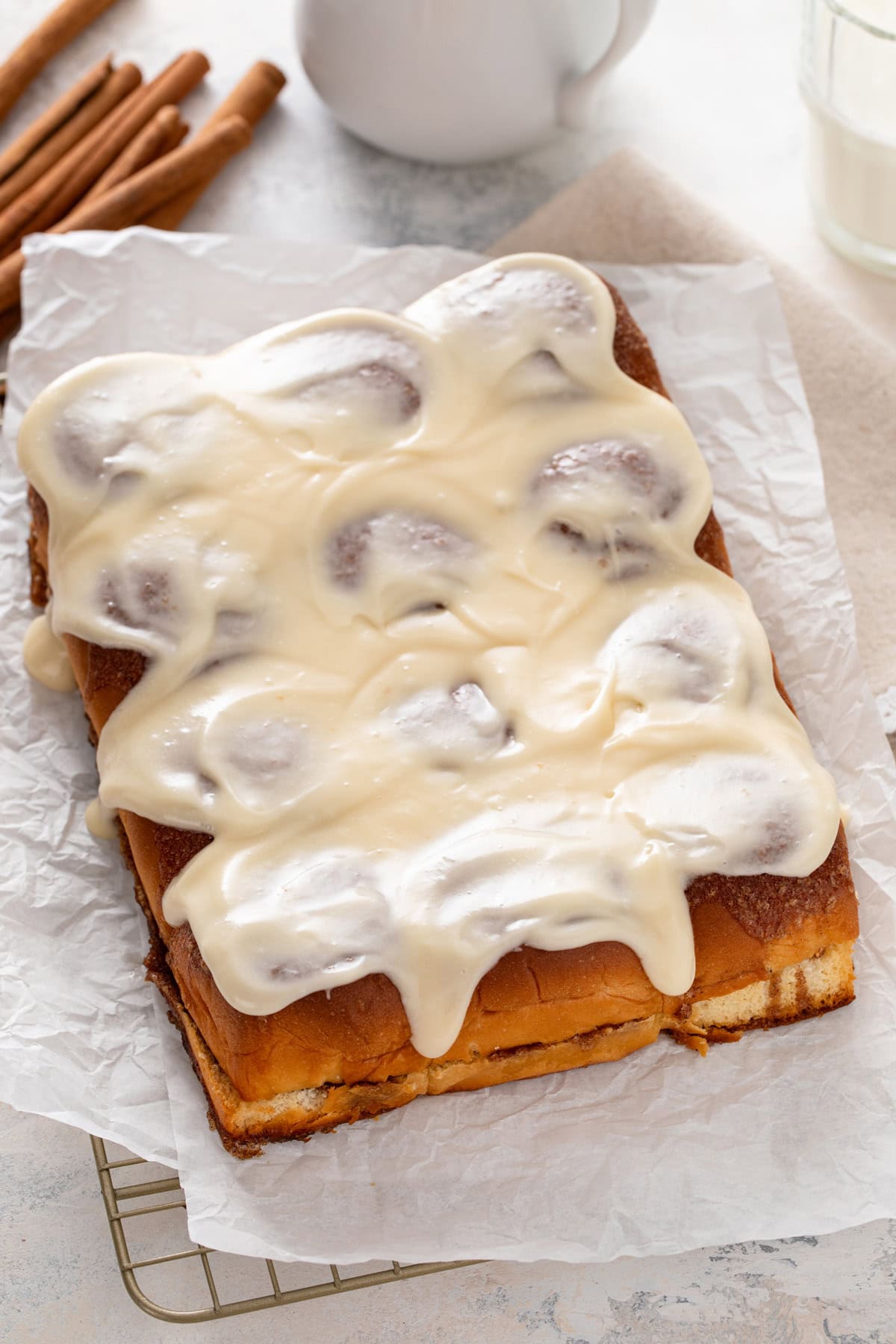 Frosted hawaiian roll cinnamon rolls on a piece of parchment paper.
