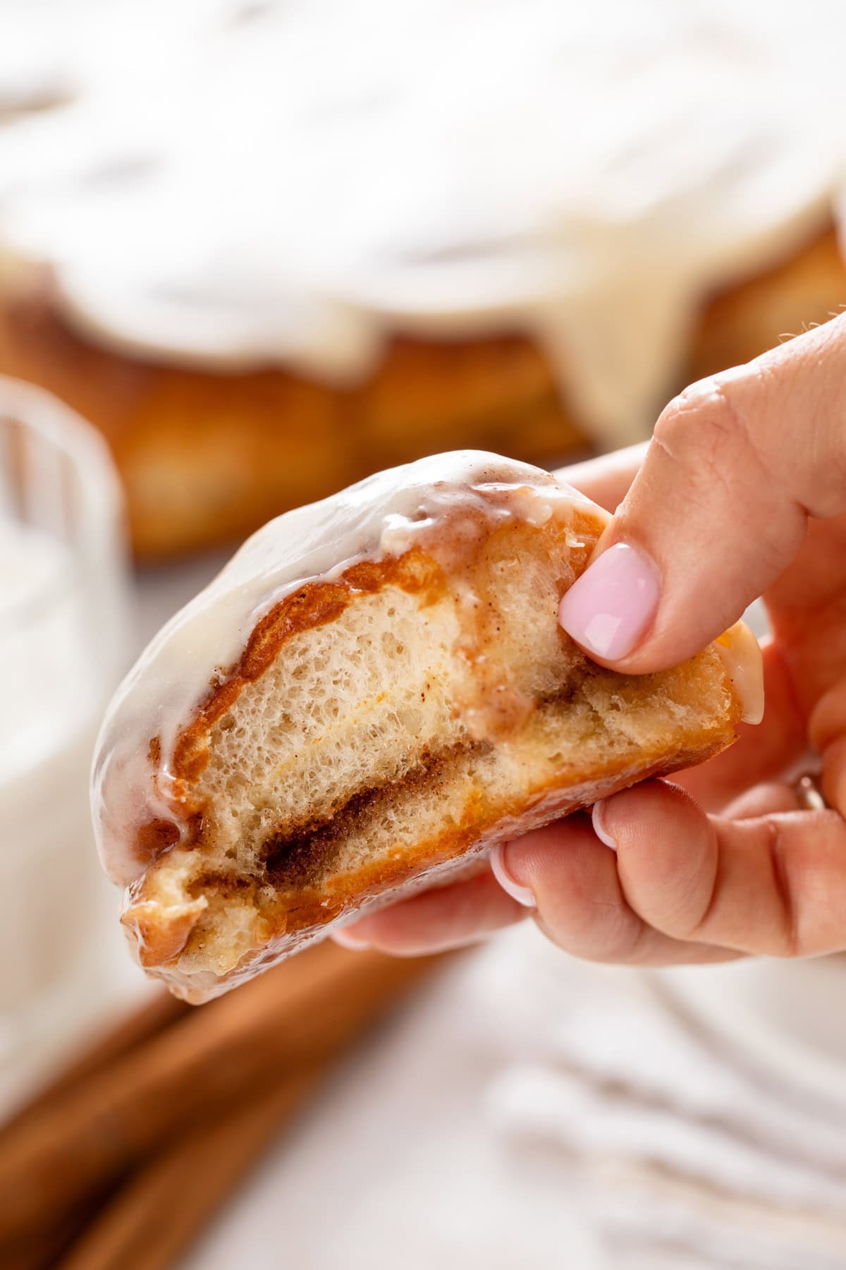 Hand holding up a hawaiian roll cinnamon roll with a bite taken from it.