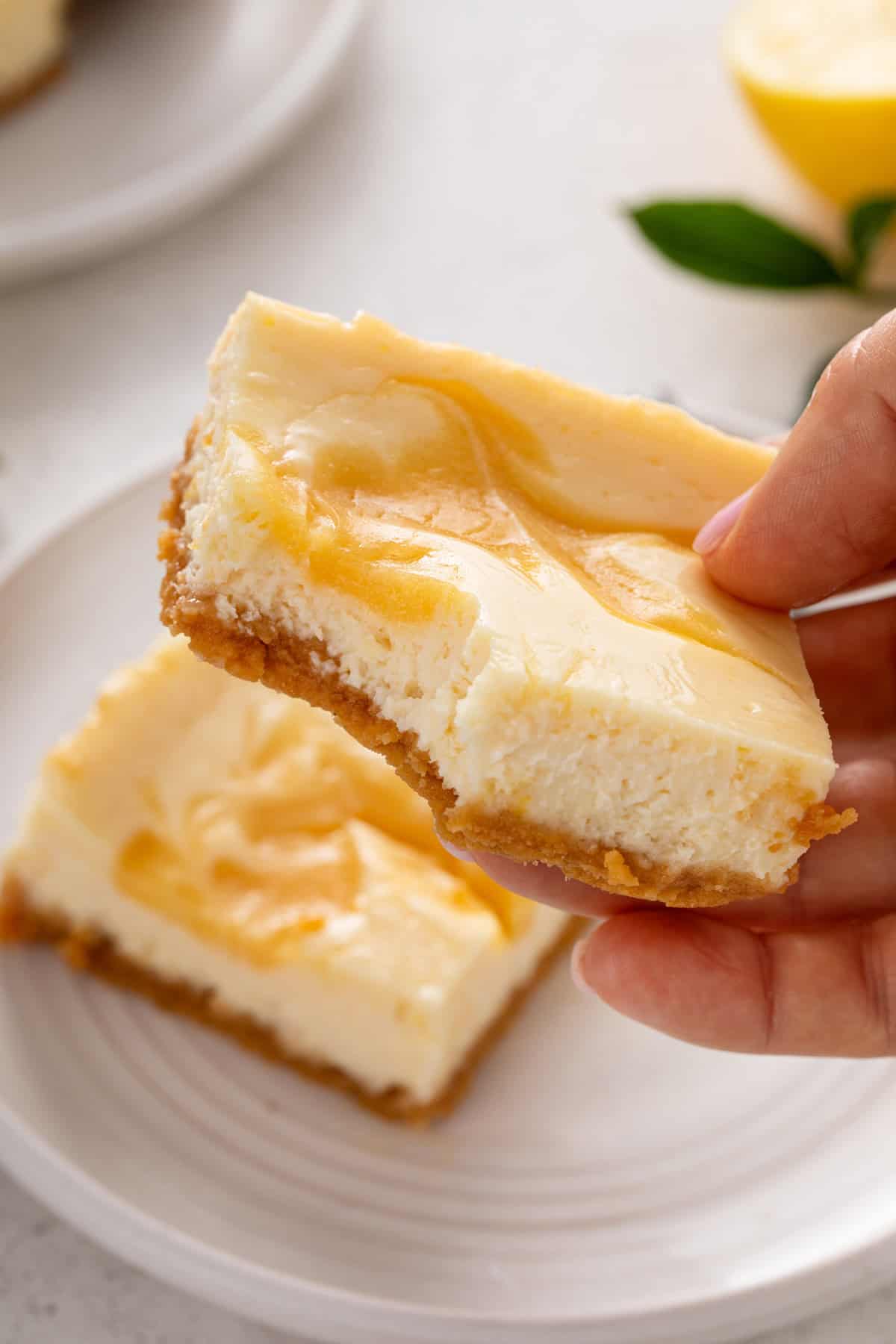 Hand holding up a lemon cheesecake bar with a bite taken from the corner.