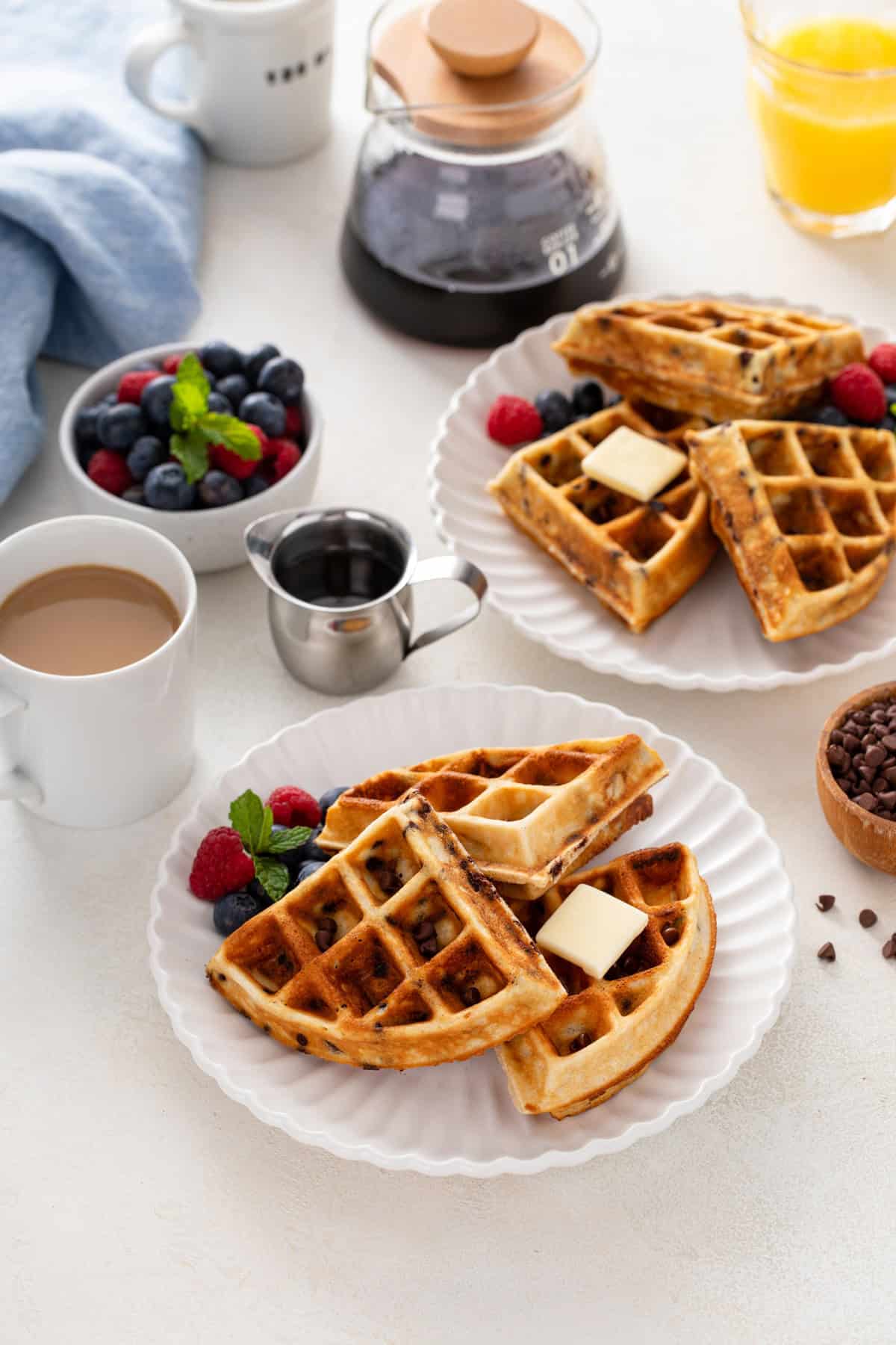 Two white plates holding buttered chocolate chip waffles.