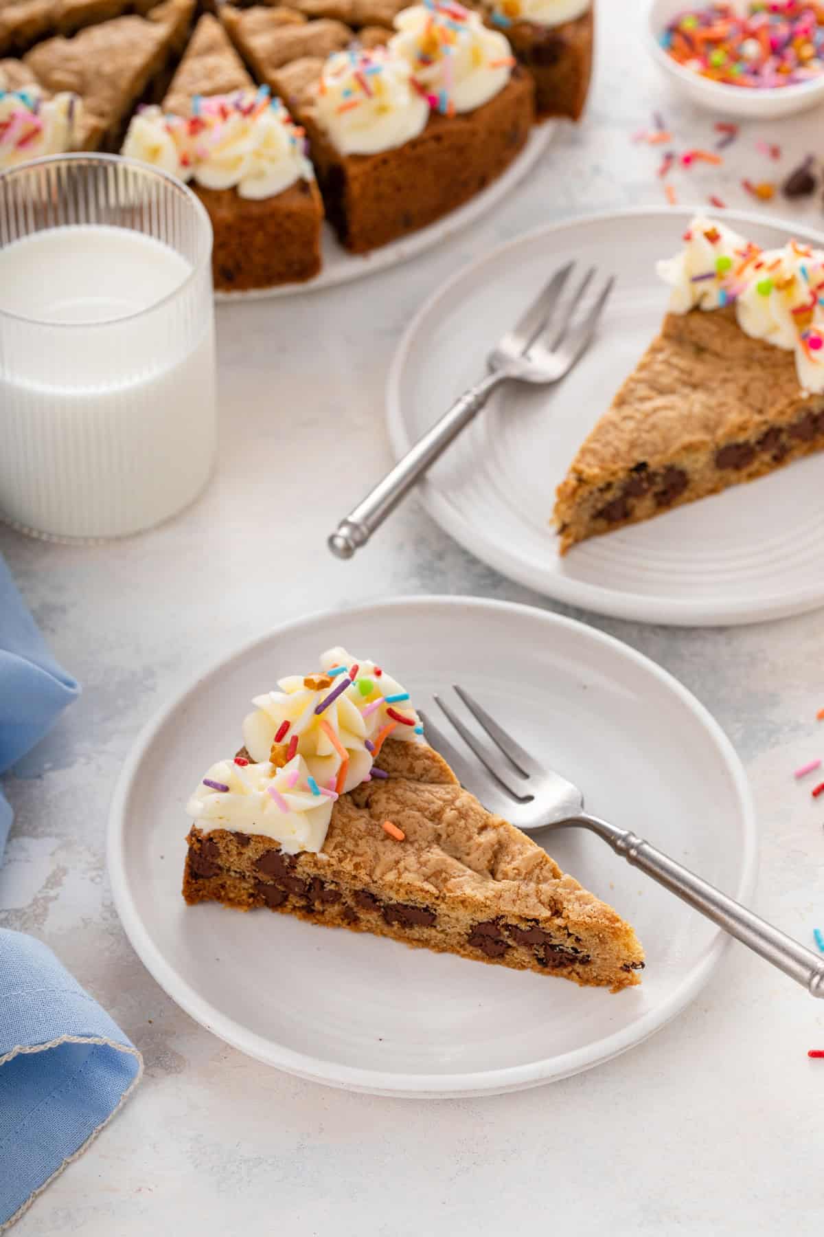 Two white plates, each holding a slice of chocolate chip cookie cake.