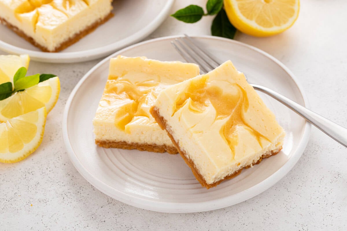 Two lemon cheesecake bars arranged next to a fork on a white plate.