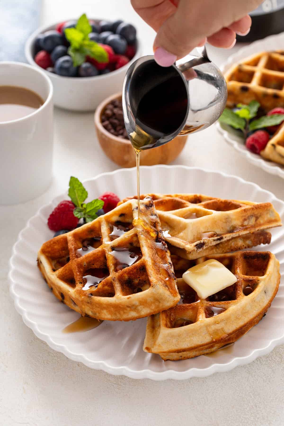 Plated chocolate chip waffles topped with butter and syrup.