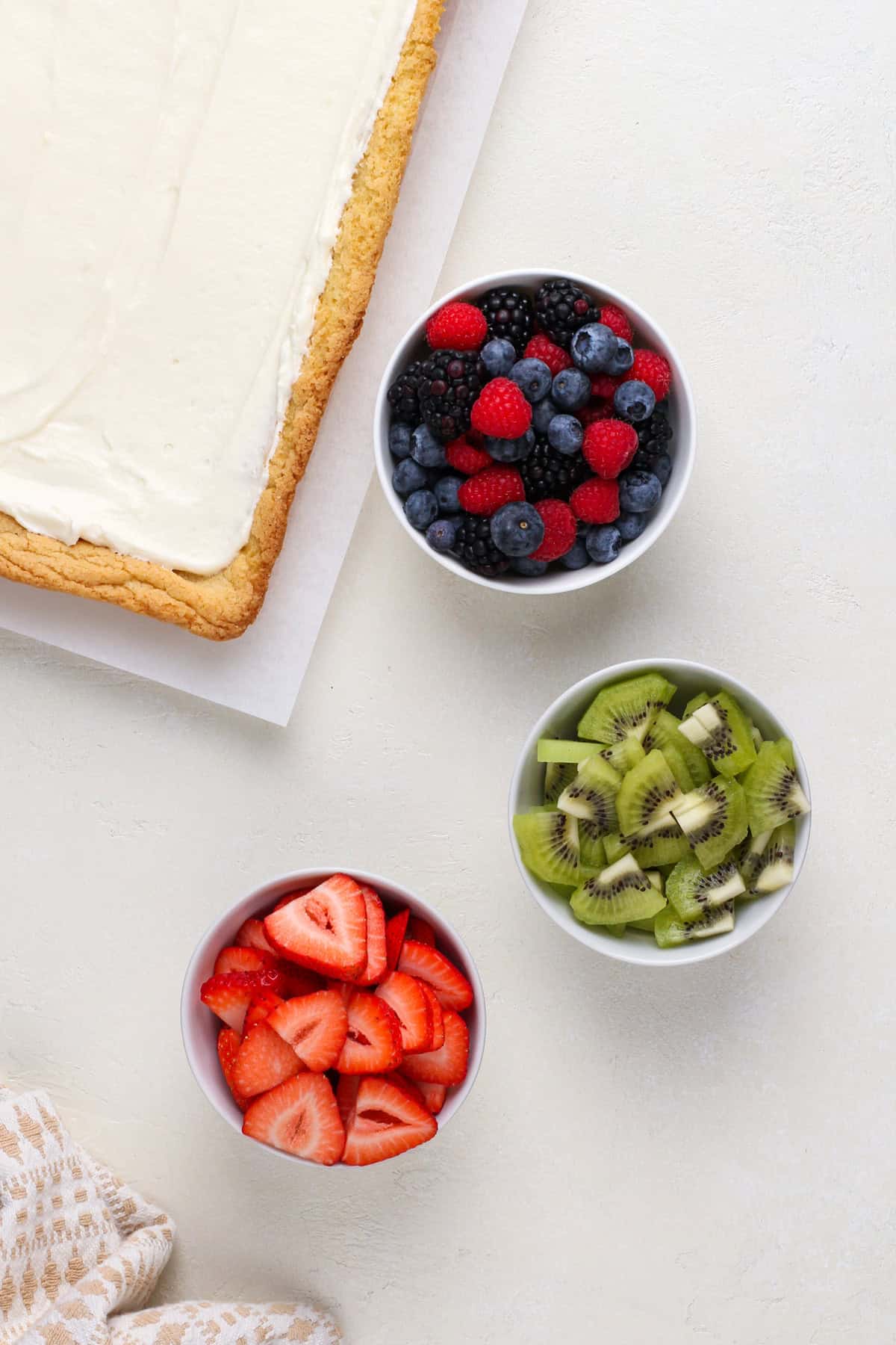 Bowls of fresh fruit next to a cookie crust topped with cream cheese filling.