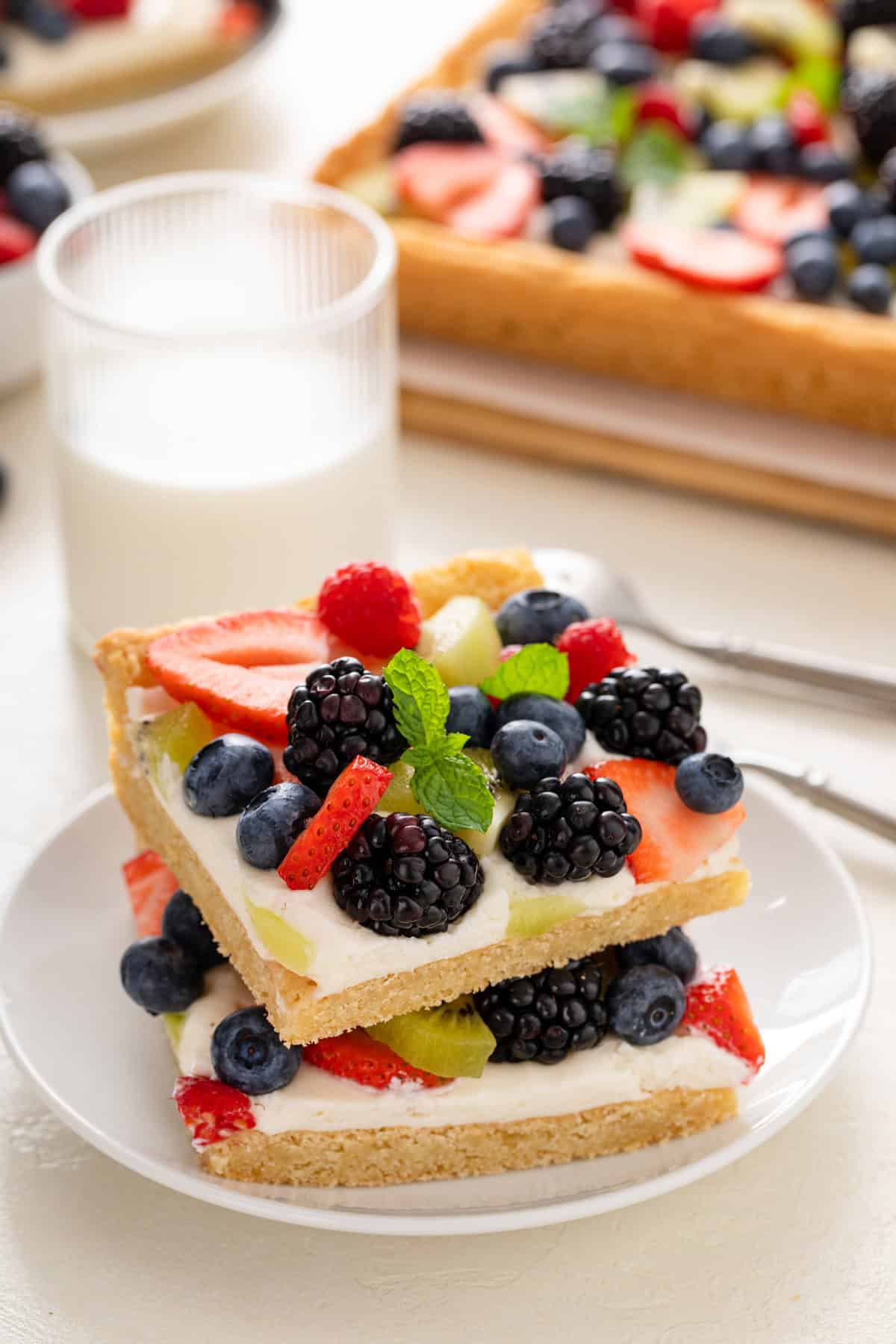 Two slices of fruit pizza stacked on a white plate.