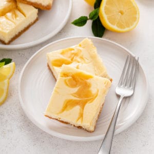Two lemon cheesecake bars on a white plate.