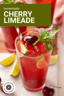 45 degree angle view of the top of a glass of cherry limeade with a straw in it. Text overlay includes recipe name.