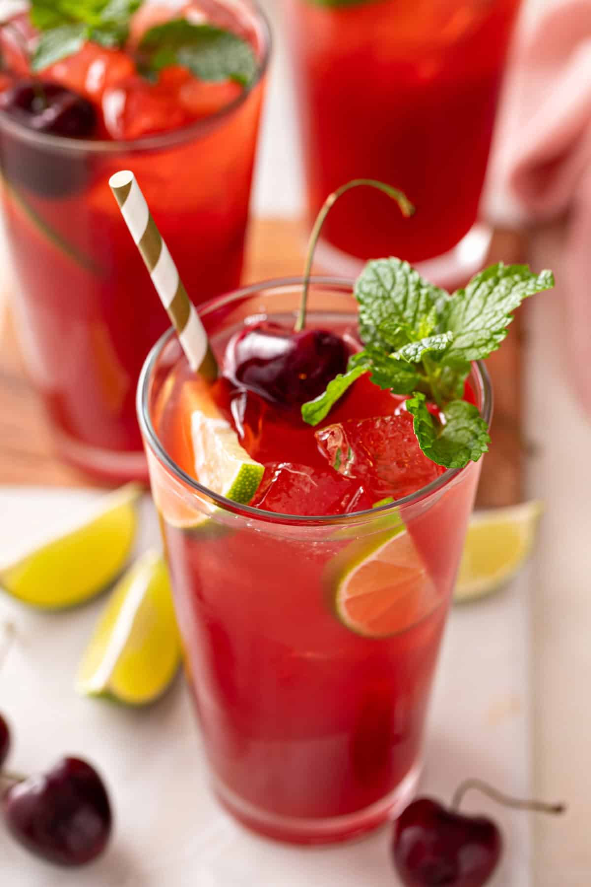45 degree angle view of the top of a glass of cherry limeade with a straw in it.