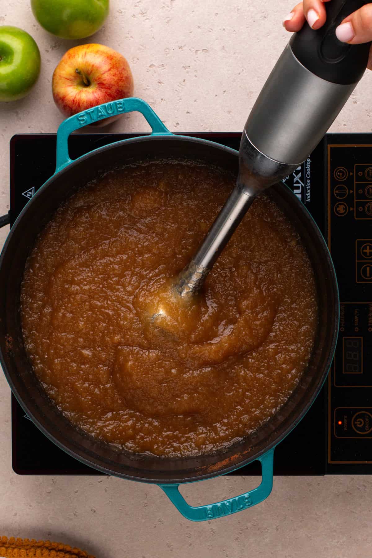 Immersion blender pureeing apple butter in a dutch oven.