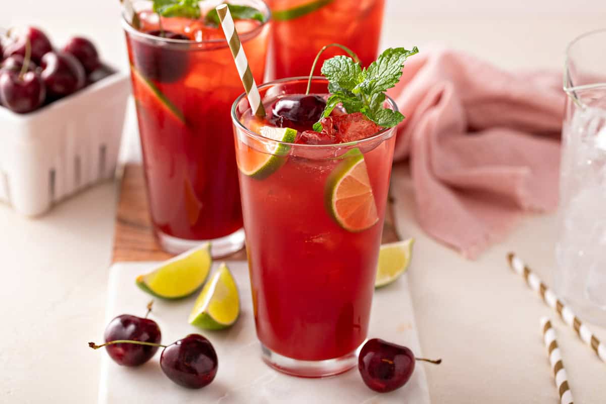 Glass filled with cherry limeade and garnished with lime, fresh cherries, and mint.