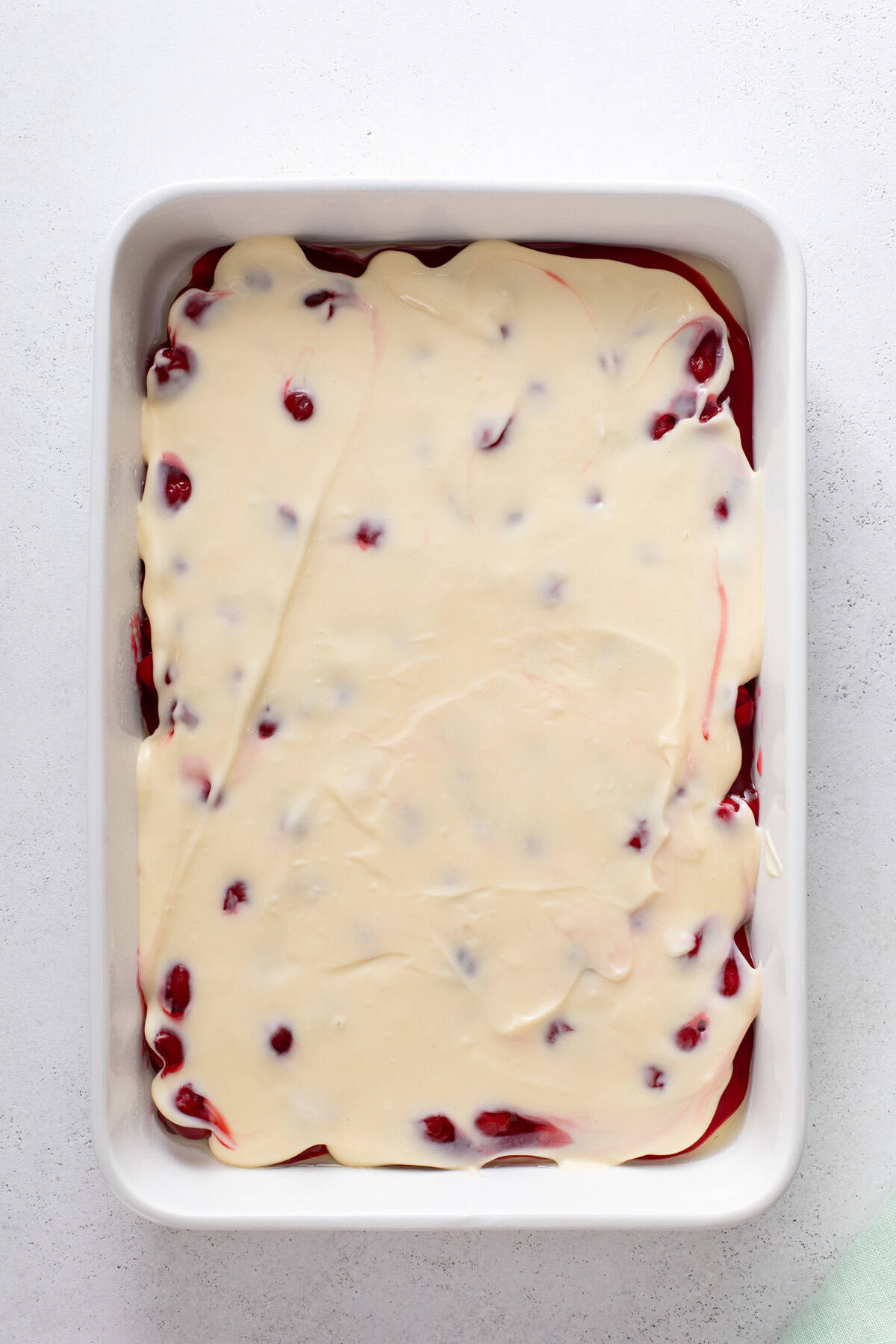 Cream cheese layer spread over cherry pie filling in a baking pan.