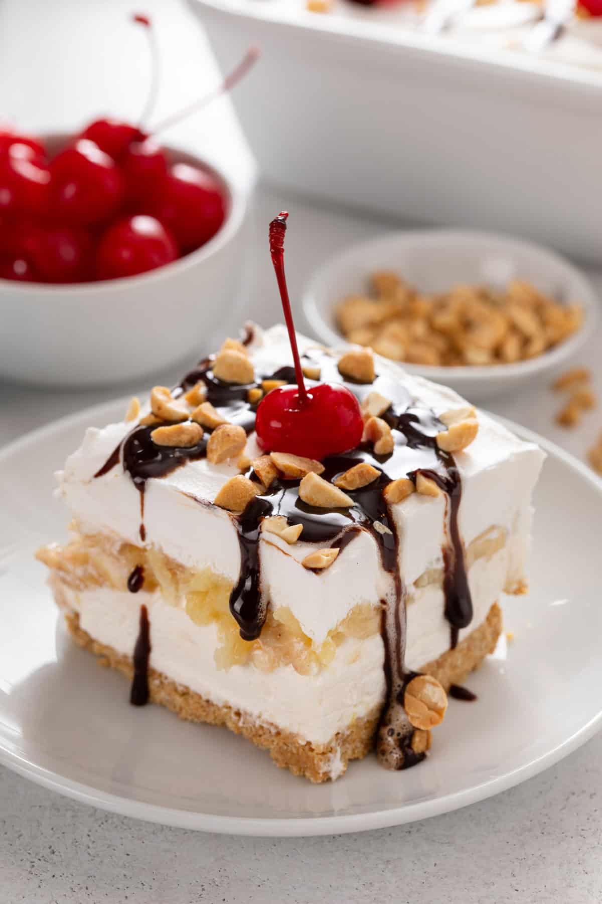 Plated slice of banana split cake topped with chocolate sauce.