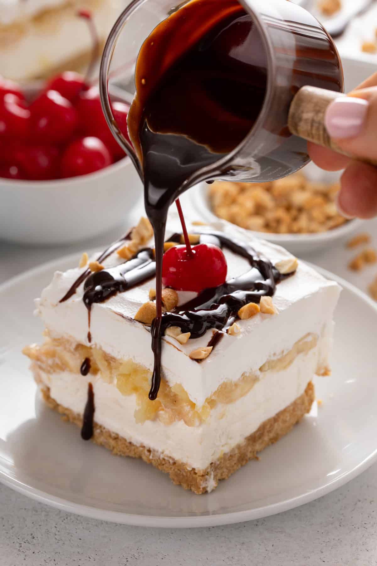 Chocolate sauce being drizzled over a slice of banana split cake.