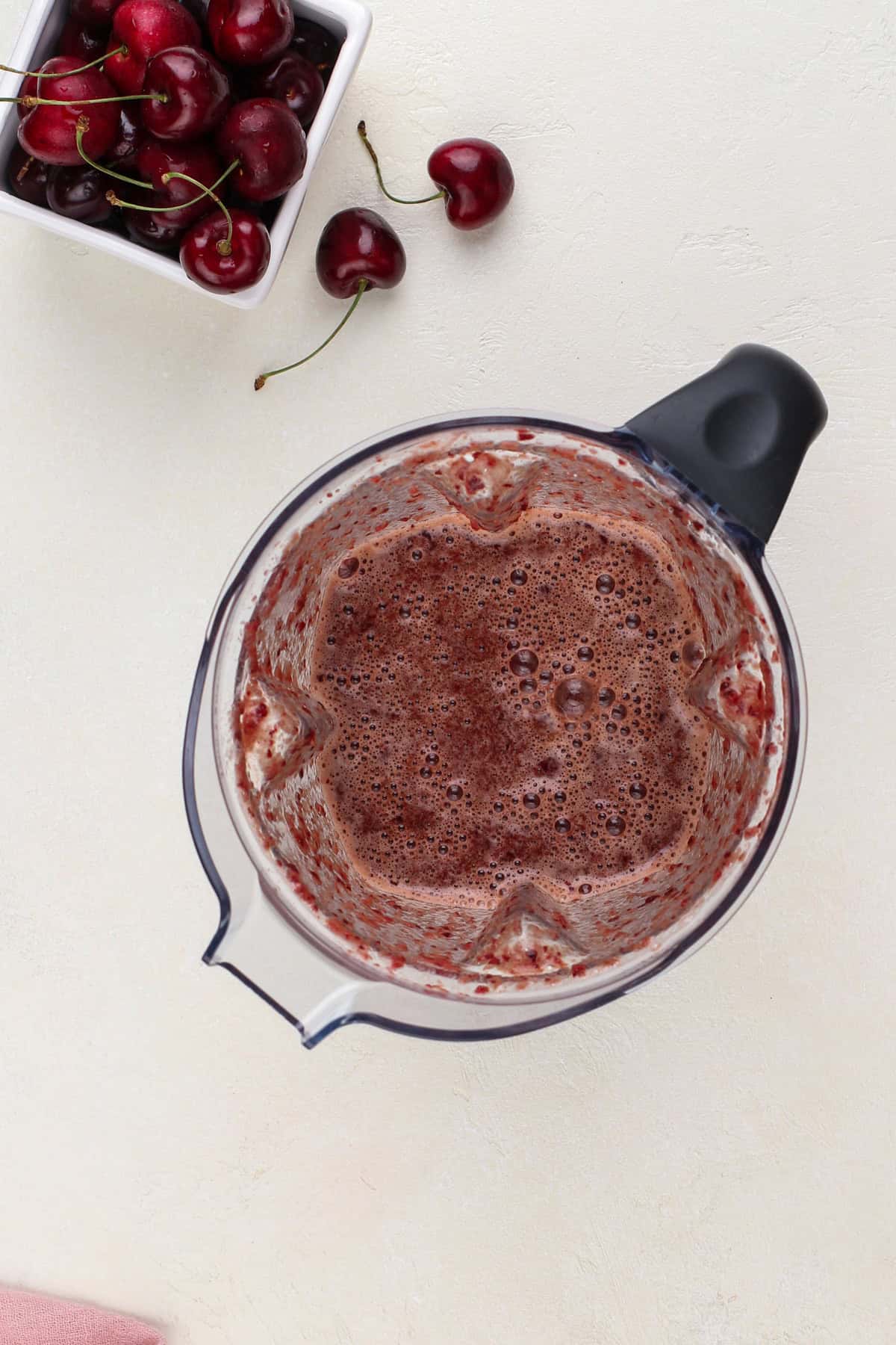 Overhead view of pureed cherries in the pitcher of a blender.