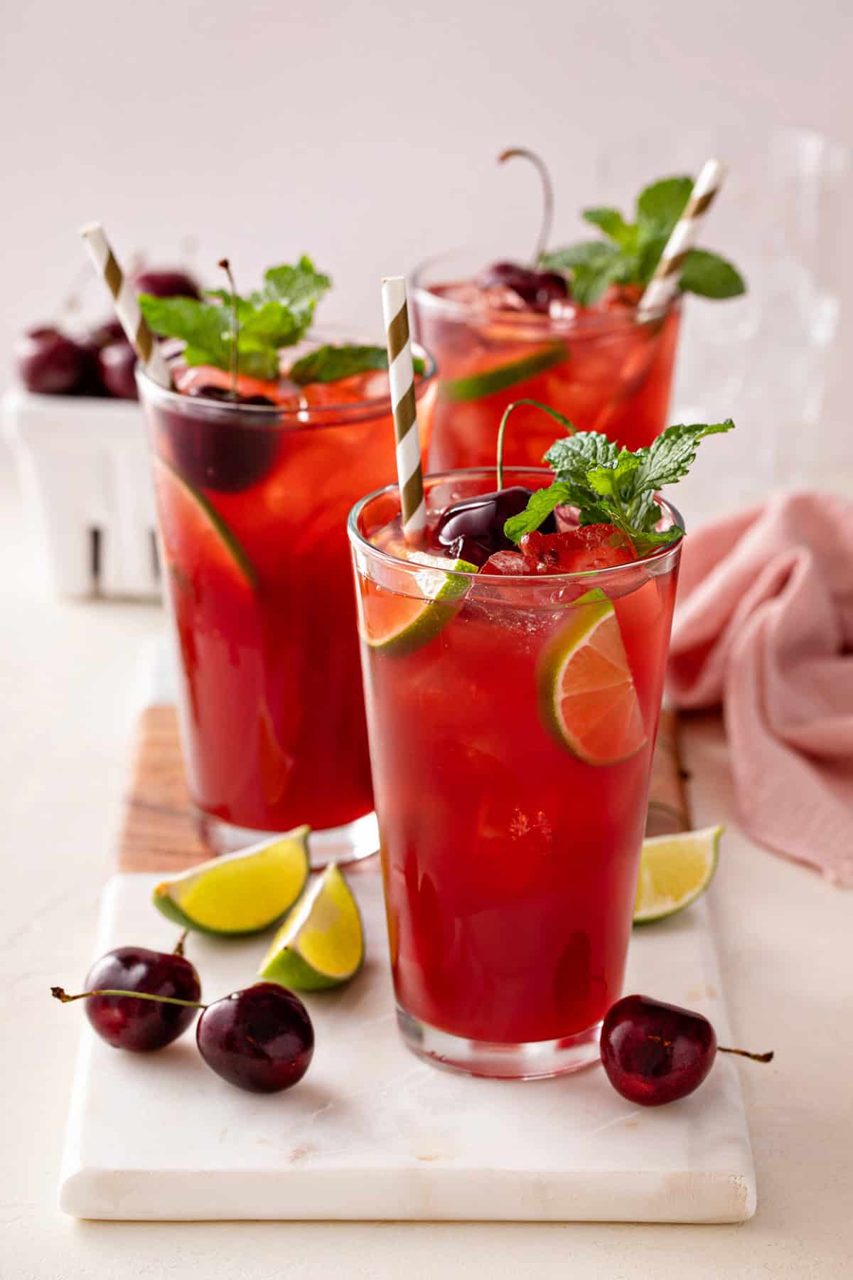 Three glasses of cherry limeade garnished with lime slices, cherries, and mint.