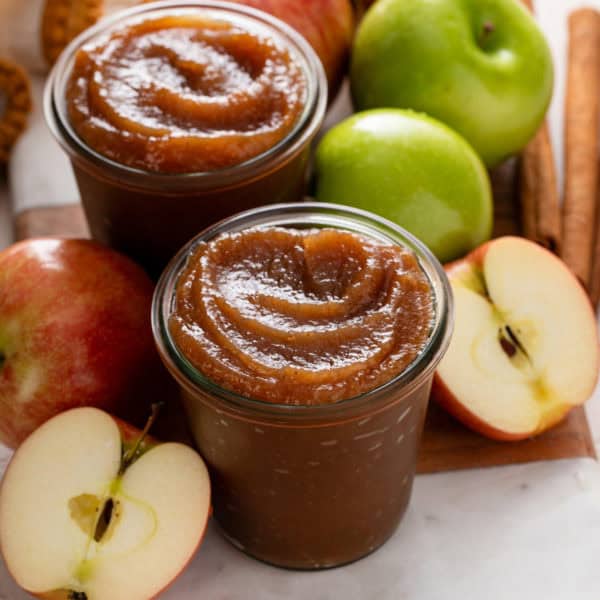 Two jars of stovetop apple butter surrounded by apples.