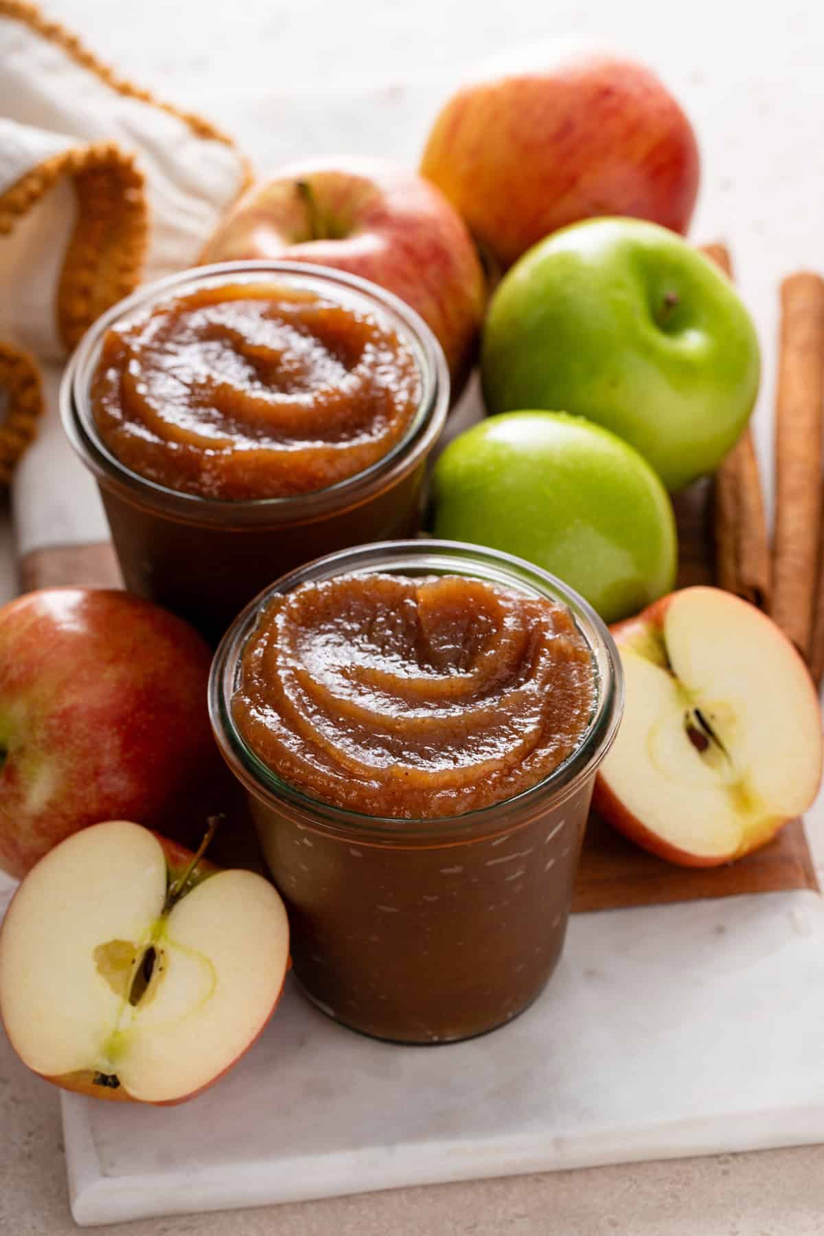 Two jars of apple butter on a countertop surrounded by apples.