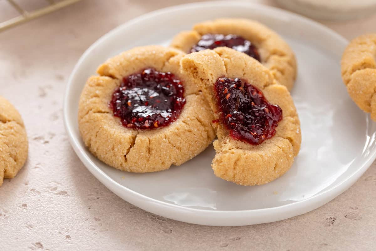 Three peanut butter and jelly cookies on a white plate, with a bite taken from the top cookie.