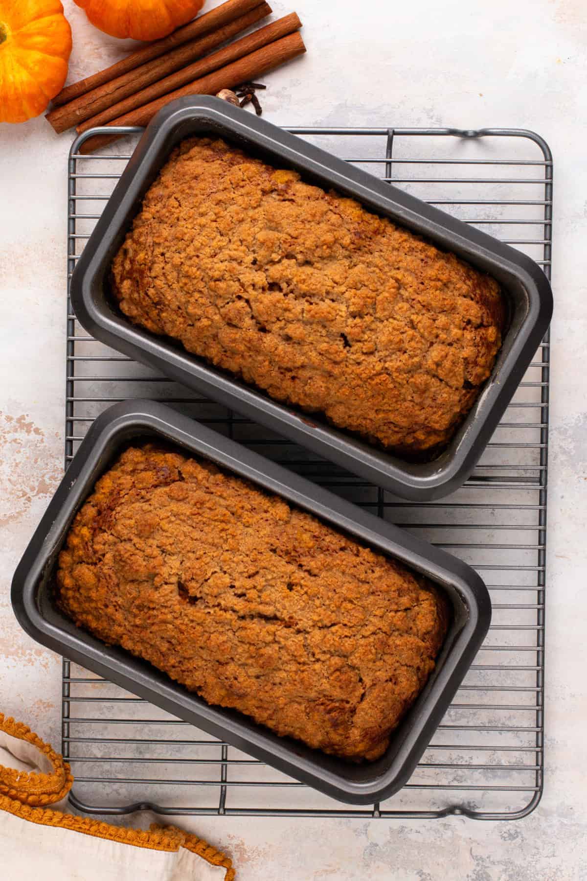 Two baked loaves of pumpkin cream cheese bread cooling on a wire rack.