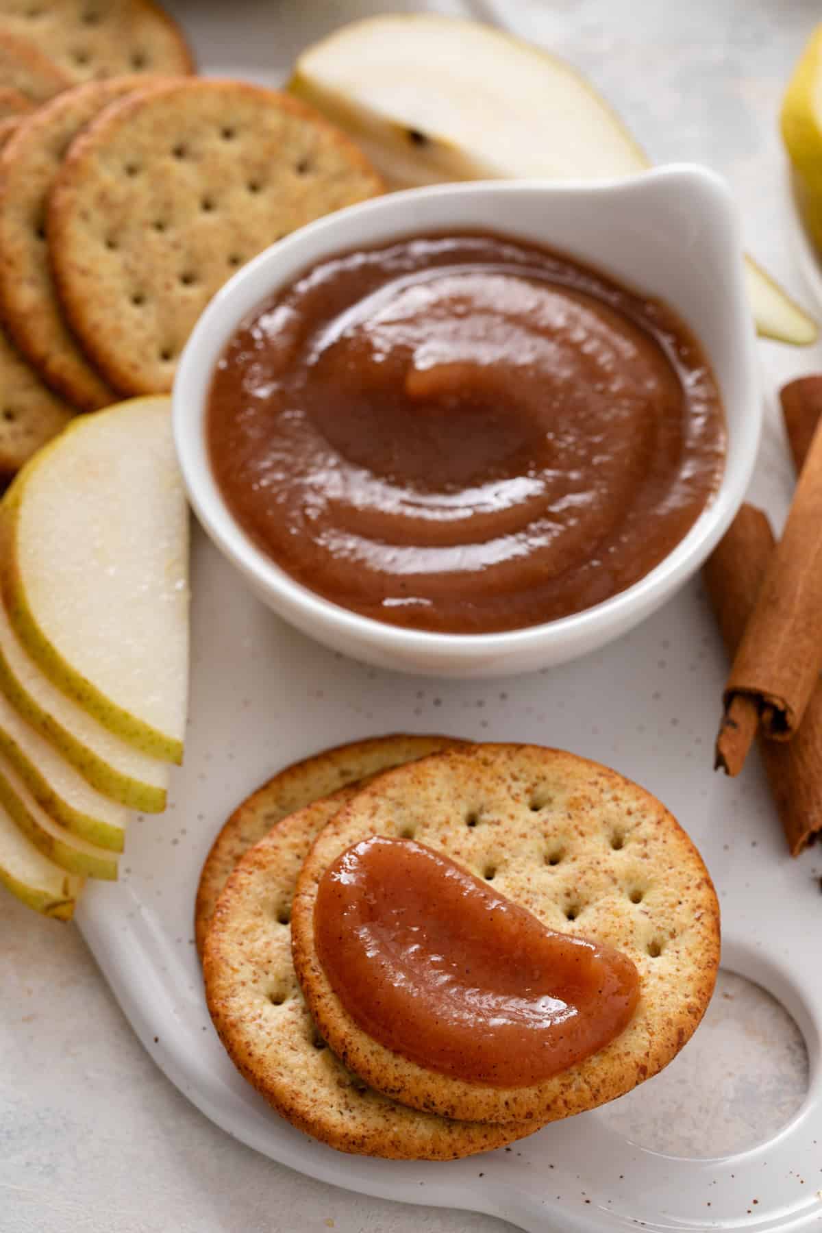 Cracker topped with pear butter next to a bowl of the pear butter.