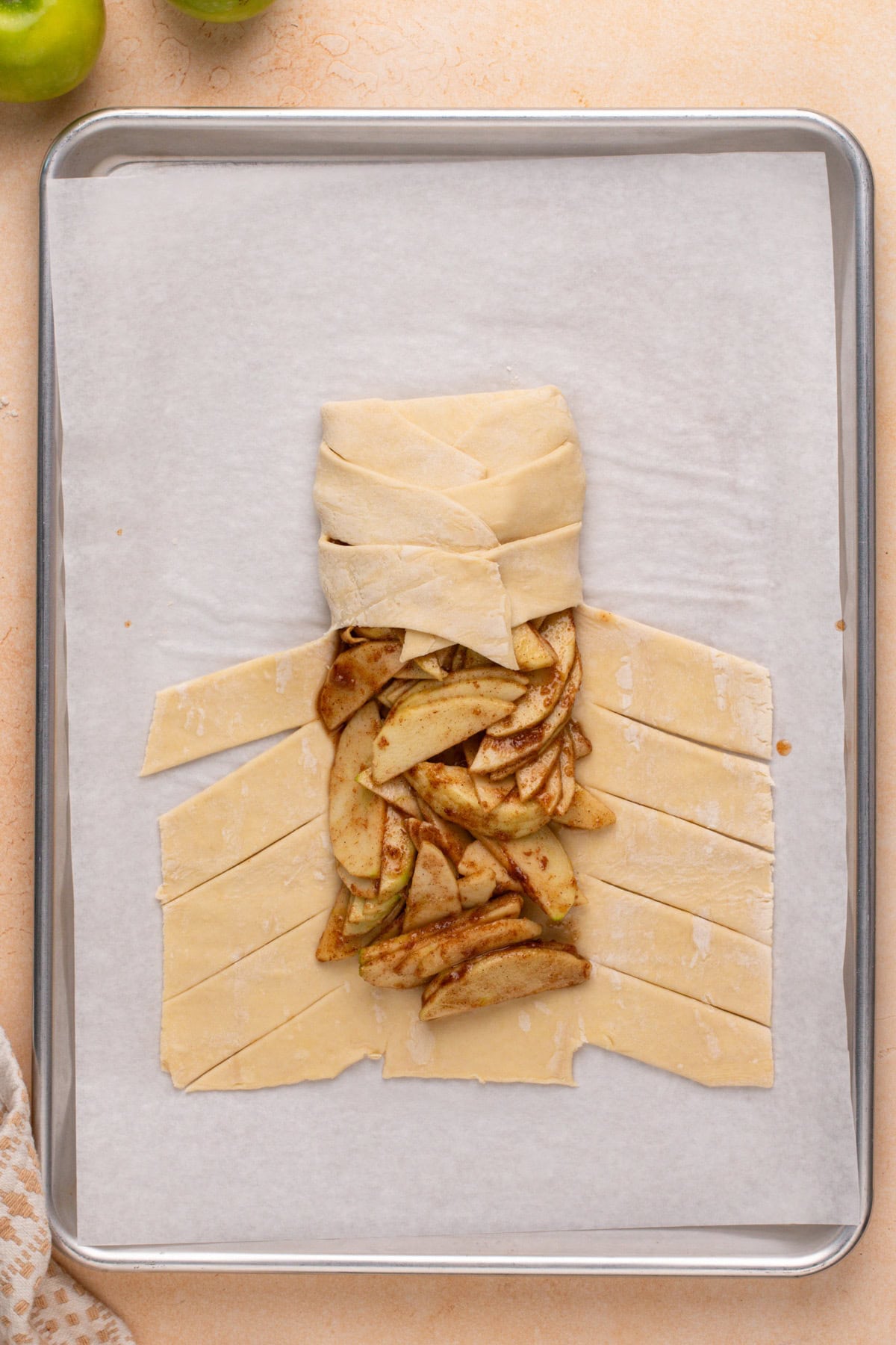 Puff pastry strips being folded over apple filling.