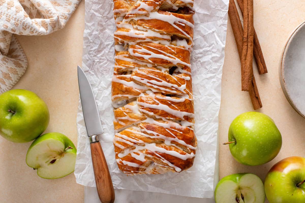 Glazed puff pastry apple strudel on a piece of parchment paper.