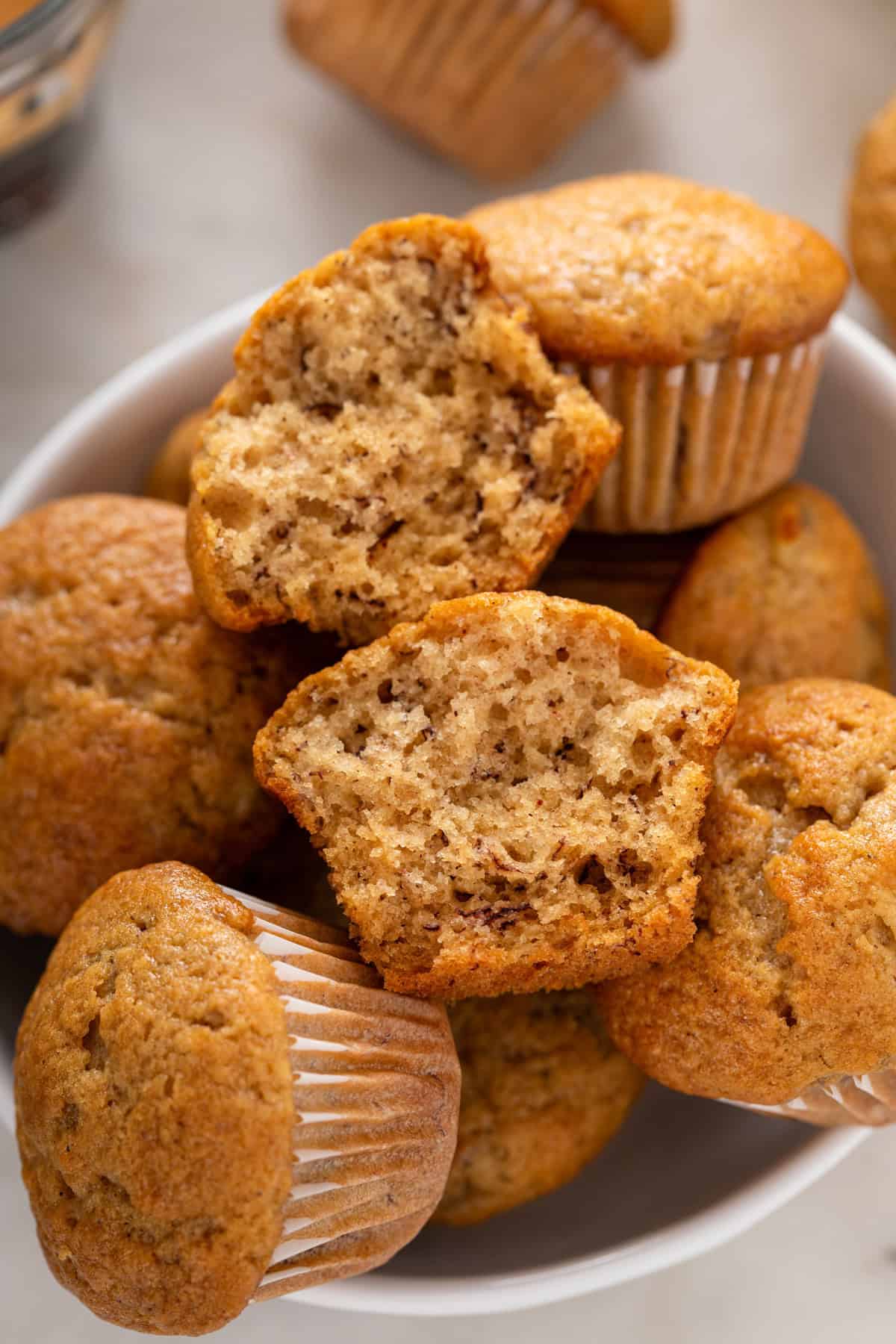 Halved mini banana muffin arranged on top of a bowl of the mini muffins.