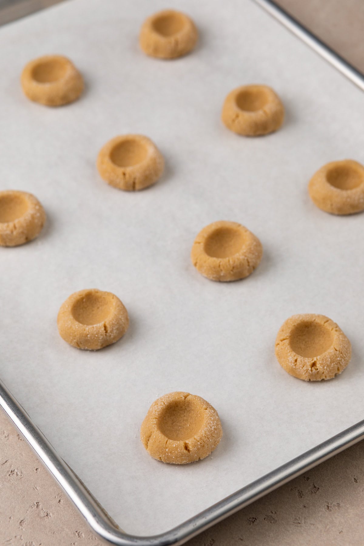Indented balls of peanut butter cookie dough on a cookie sheet.