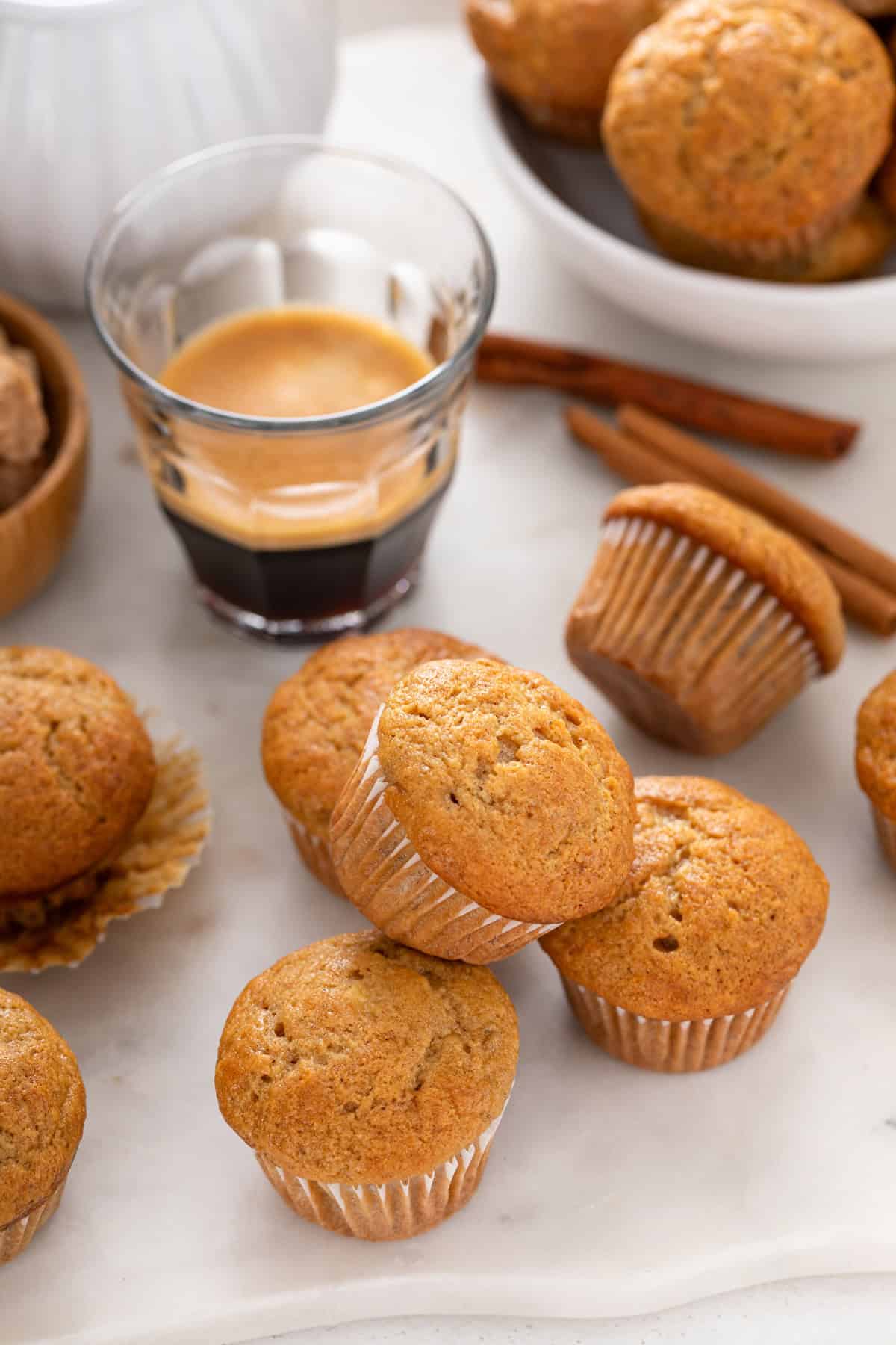 Mini banana muffins scattered on a countertop in front of a glass of espresso.