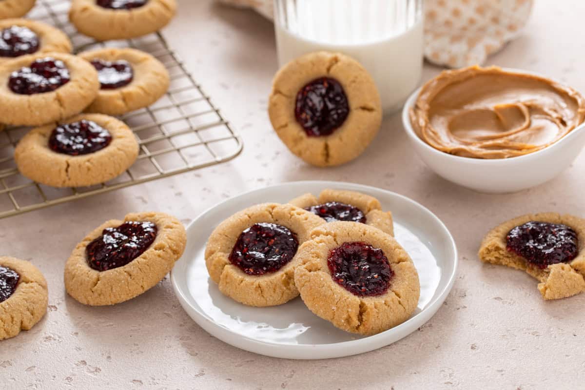 Peanut butter and jelly cookies arranged on a plate and wire rack with a glass of milk in the background.