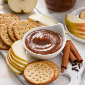 Small bowl of pear butter surrounded by crackers and sliced pears.