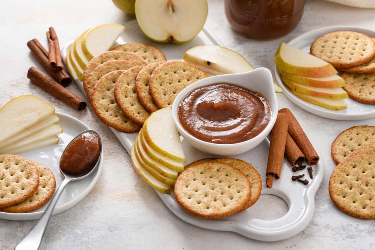 White board topped with crackers, sliced pears, and a bowl of pear butter.