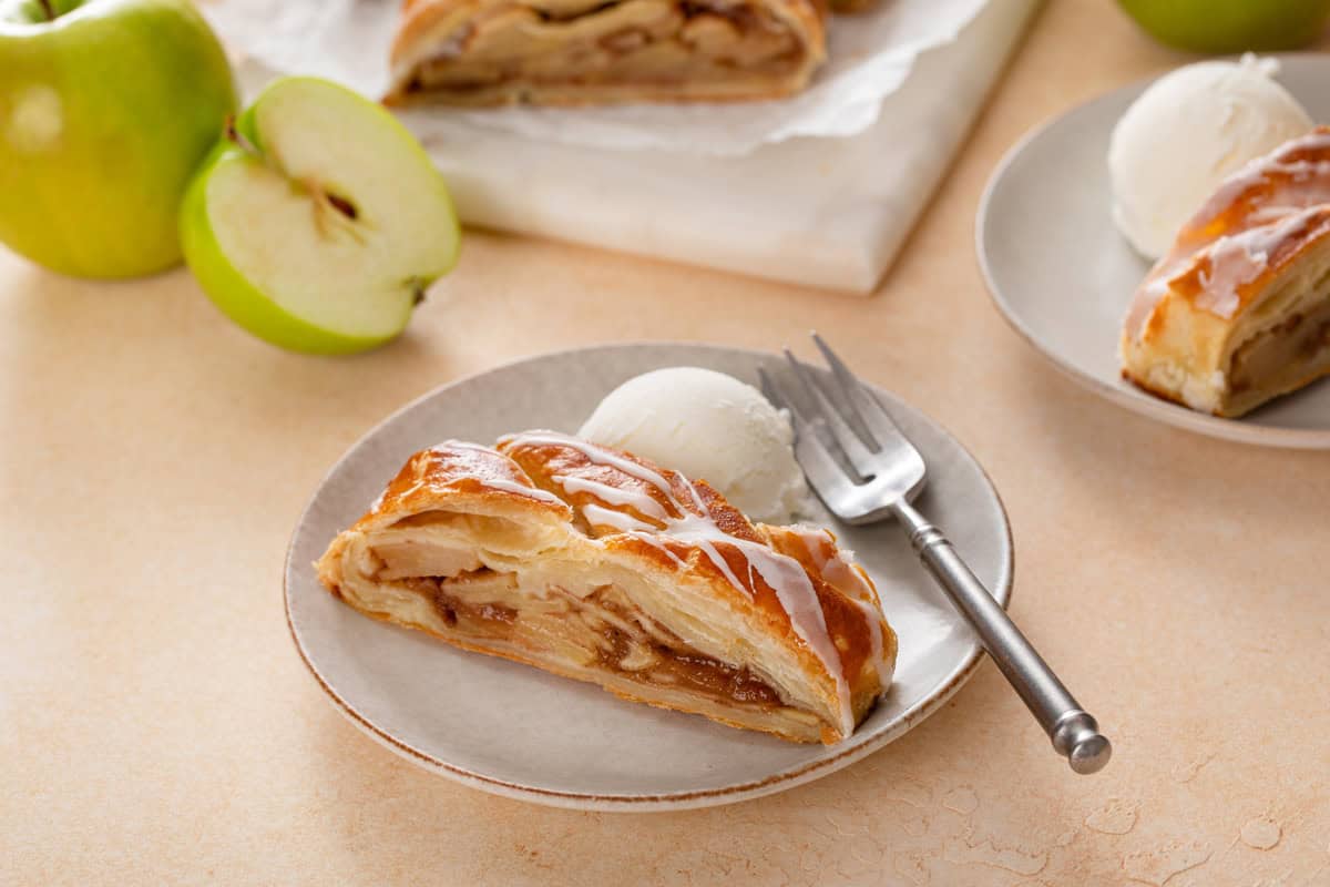 Plated slice of puff pastry apple strudel next to a scoop of ice cream.