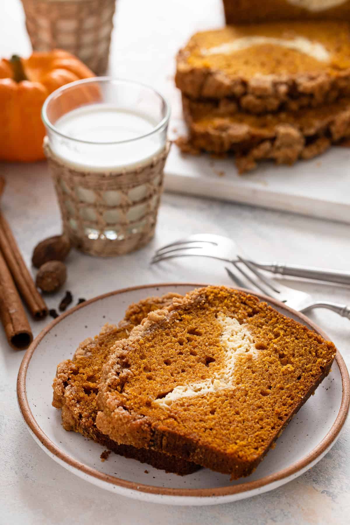 Plate of pumpkin cream cheese bread in front of a glass of milk.