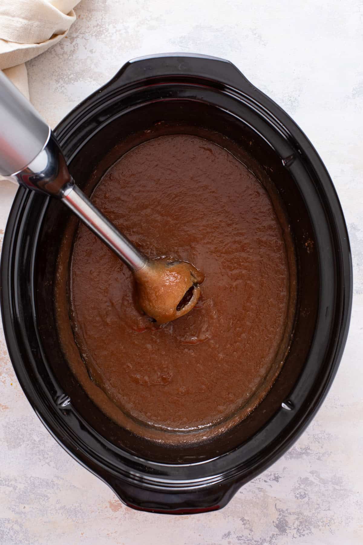 Immersion blender pureeing pear butter in the crock of a slow cooker.