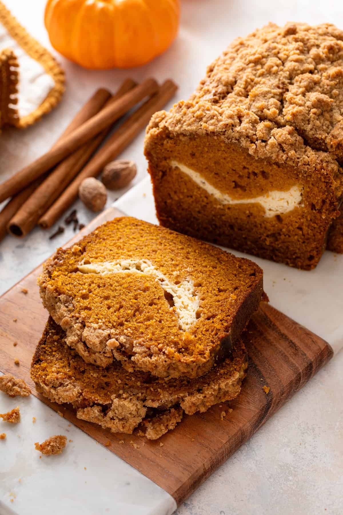 Sliced loaf of pumpkin cream cheese bread on a marble and wood board.