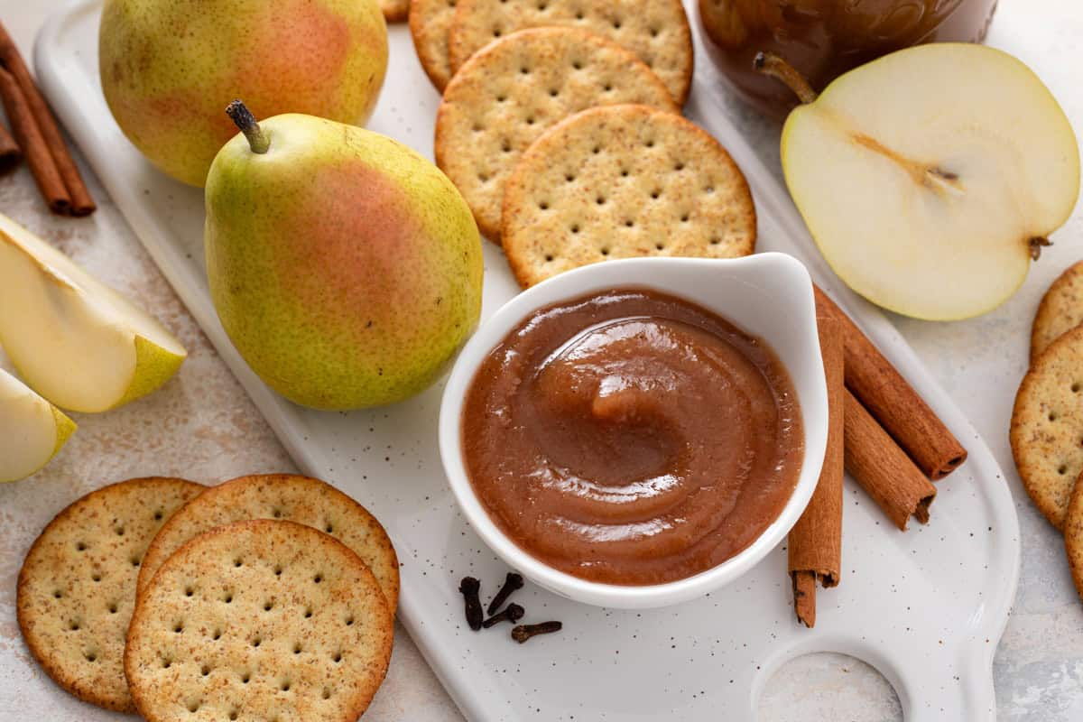 Pear butter in a small bowl next to crackers and whole pears.