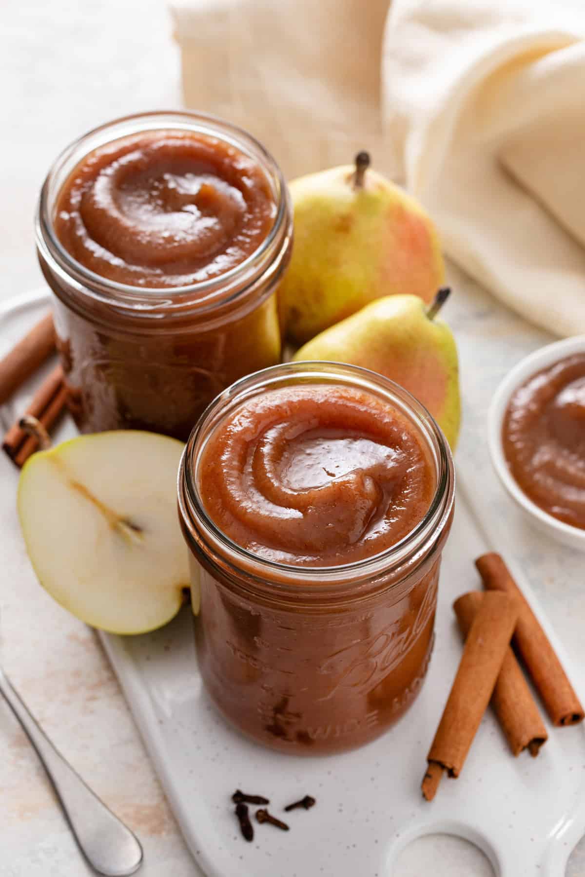 Two jars filled with pear butter surrounded by spices and fresh pears.