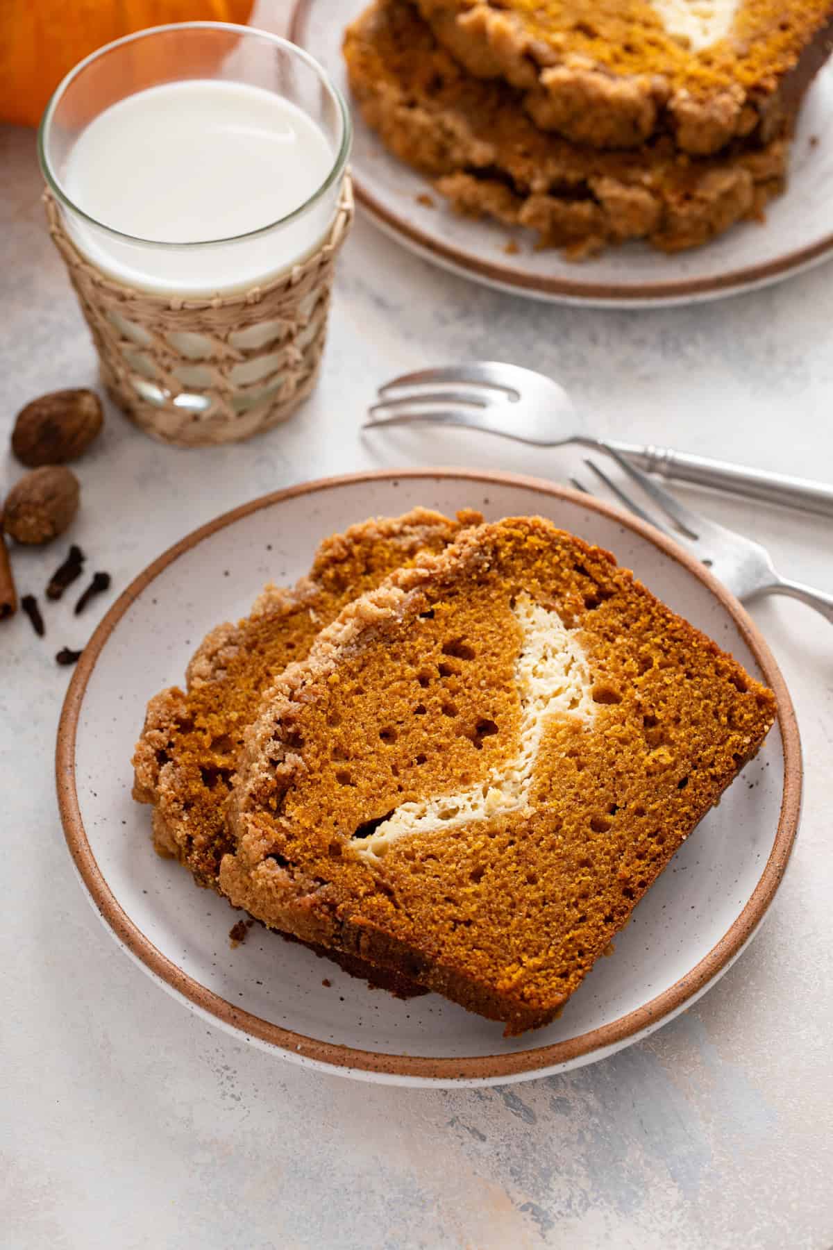 Two slices of pumpkin cream cheese bread on a plate in front of a glass of milk.